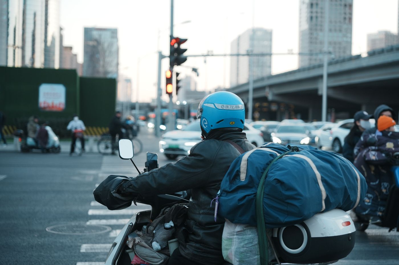国内城市街景中的外卖骑手，戴头盔、车后带配送箱